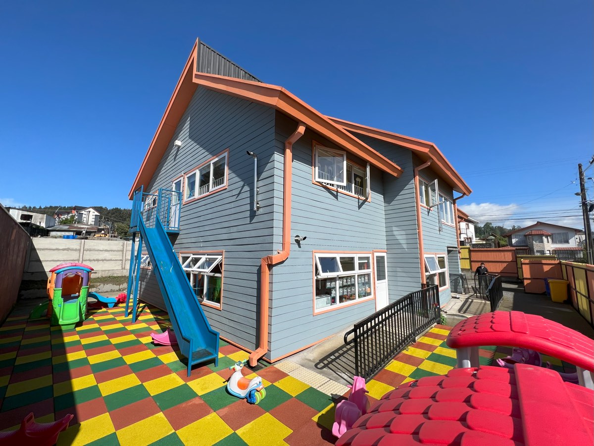 Patio de juegos del Jardín Infantil Ardillitas, con toboganes y suelo de colores frente al edificio